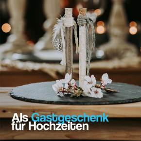 Elegante Reagenzgläser mit Verschluss, dekoriert mit Feder und Jute als Tischdekoration für eine Hochzeit.