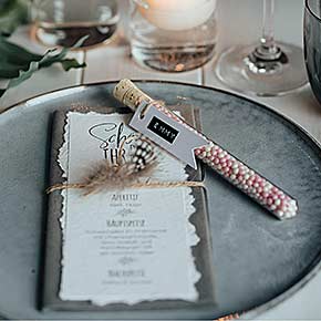 Reagenzglas befüllt mit Zuckerperlen und Namensanhänger auf Teller für Hochzeit